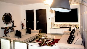 A modern living room with a sofa, a coffee table, a chandelier, and a flat-screen TV. - Immaculate Beauty Gem Location Pools Gym (Accra)