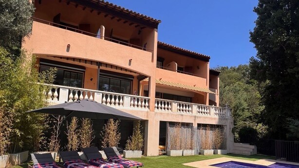 Una casa a due piani con piscina, un patio coperto con poltrone relax e un balcone.