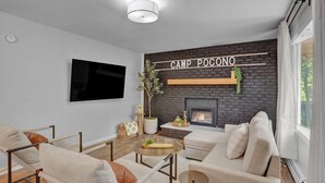 Ein modernes Wohnzimmer mit Kamin, einem Wand-Fernseher und einem Schild mit der Aufschrift 'CAMP POCONO'.