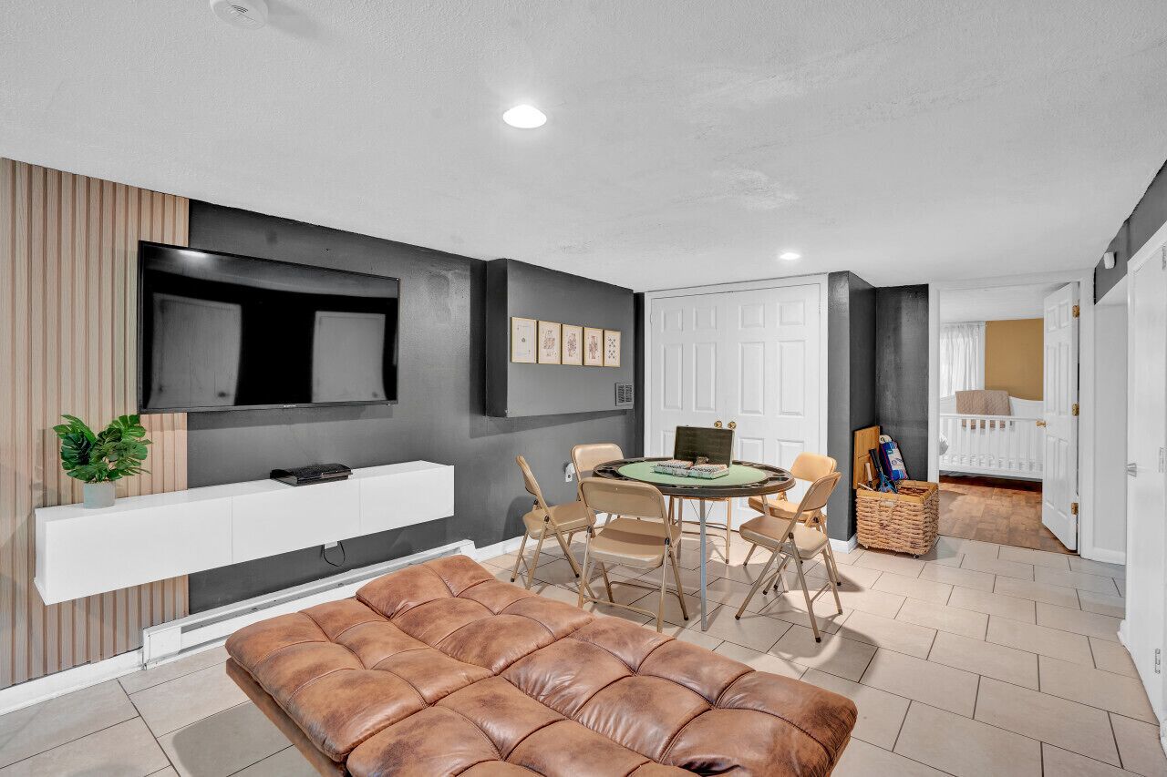 Een moderne woonkamer met een flatscreen televisie, een bruine leren bank, een eettafel met stoelen en een witte console tafel.