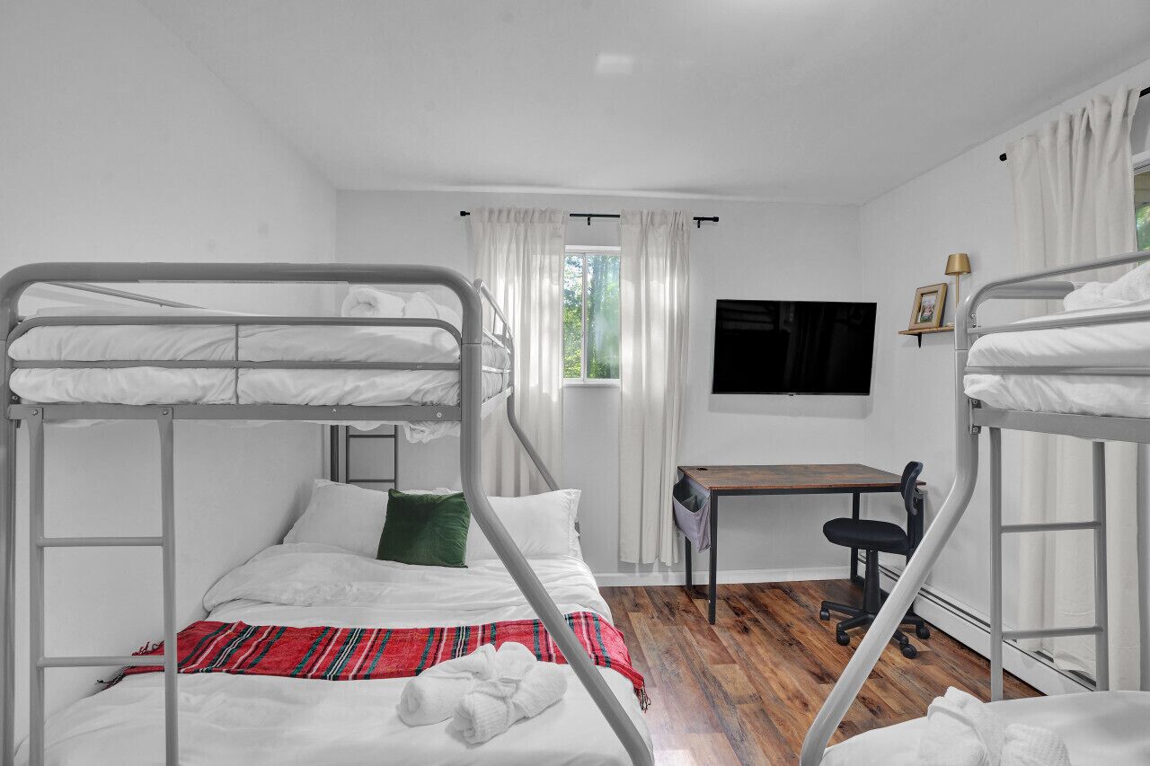 Une chambre de dortoir avec des lits superposés, un bureau, une chaise et un téléviseur fixé au mur.