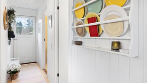 Een hal met een witte deur, een mand met witte bloemen en een wandplank met verschillende borden.