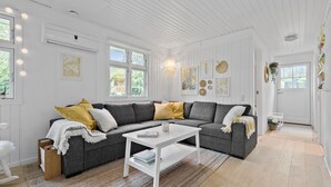 Een moderne woonkamer met een grijze modulaire bank, een witte salontafel en een groot raam dat voor natuurlijk licht zorgt.