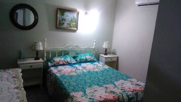 Un dormitorio con una cama, dos mesitas de noche, un atril y un aire acondicionado instalado en la pared.