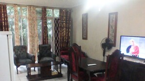 A living room with a dining table, chairs, a television, and a fan.