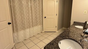 Een badkamer met twee wastafels, een douche met een patroondouchegordijn en een deur met een hendel.