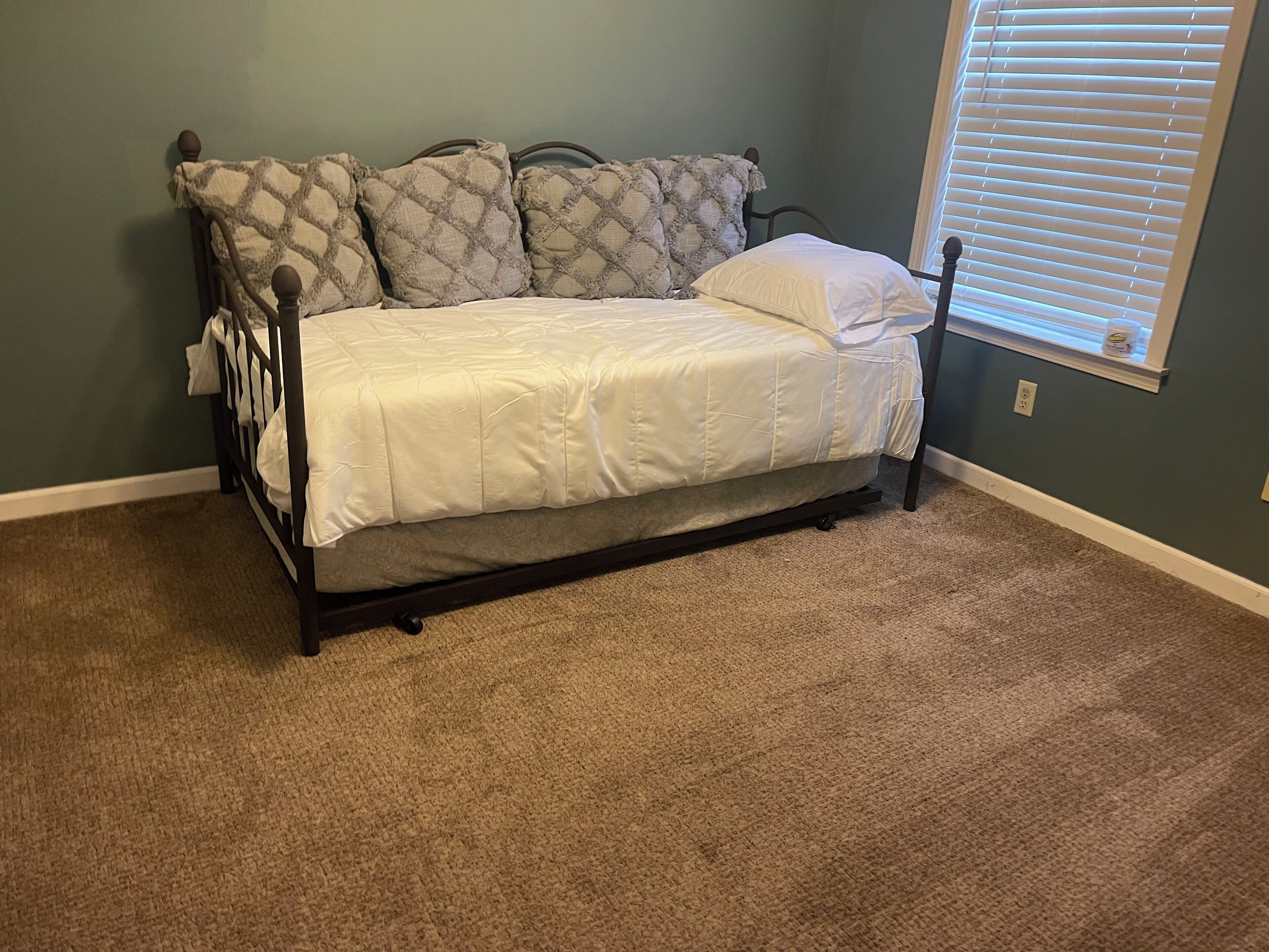 A bedroom with a bed, a window with blinds, and a carpeted floor.