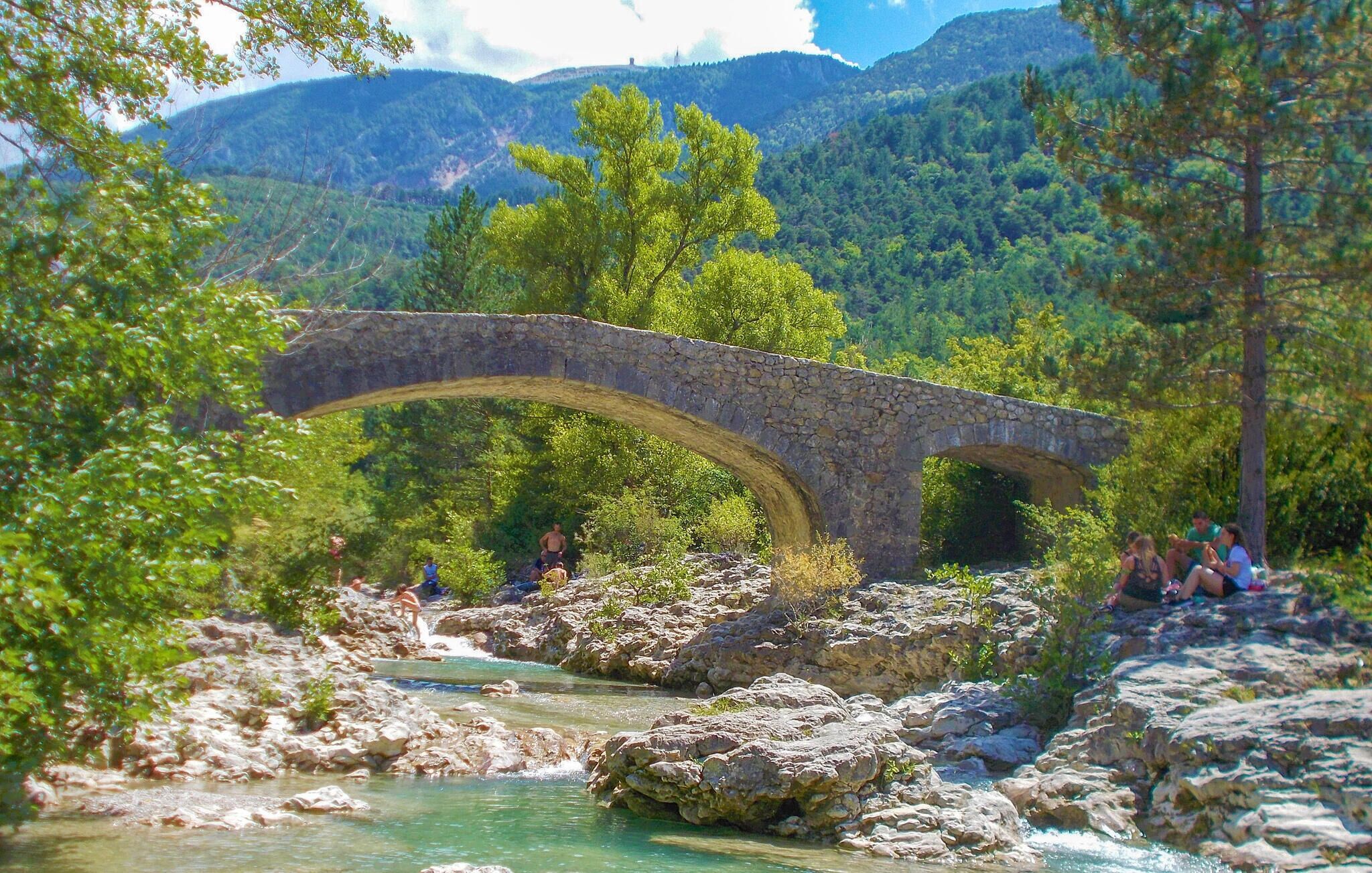 A stone bridge over a river with people walking nearby.