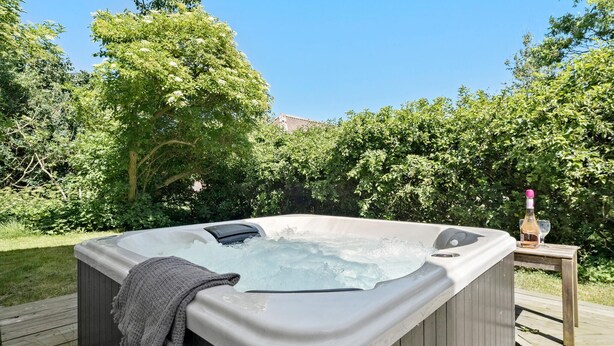 Ein Whirlpool auf einer Holzterrasse, umgeben von üppiger Vegetation.