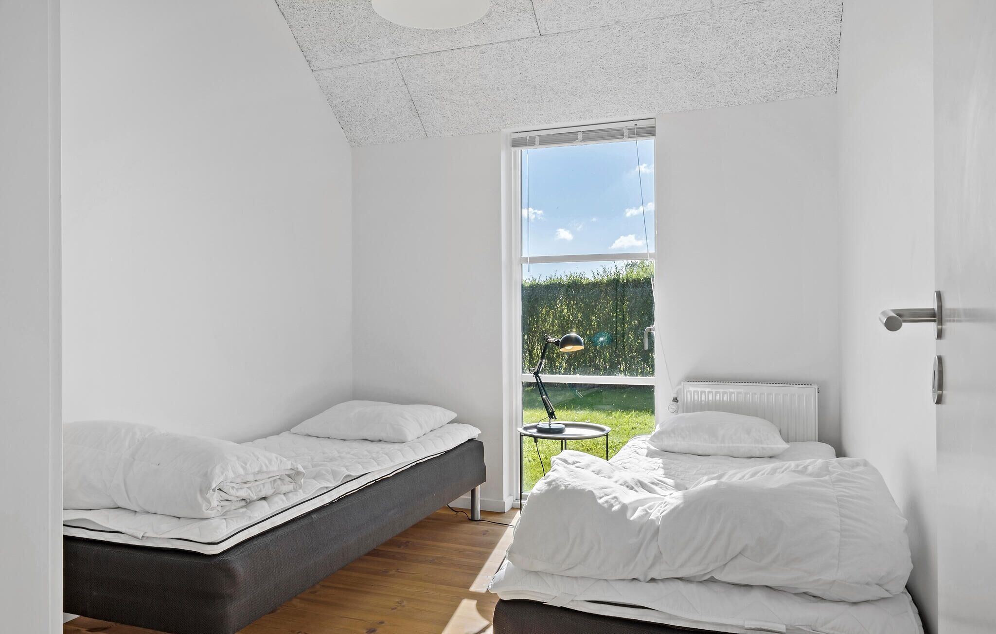 A small, bright room with two beds, a window, and a radiator.
