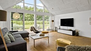 Ett rymligt vardagsrum med ett stort fönster, en platt-TV och en modern soffa.