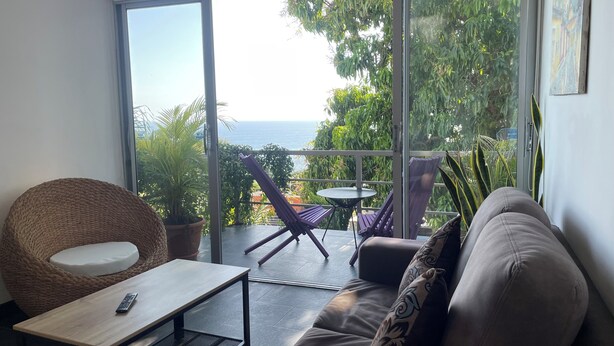 Un balcon avec vue sur la mer, aménagé avec un canapé, une chaise et une petite table.