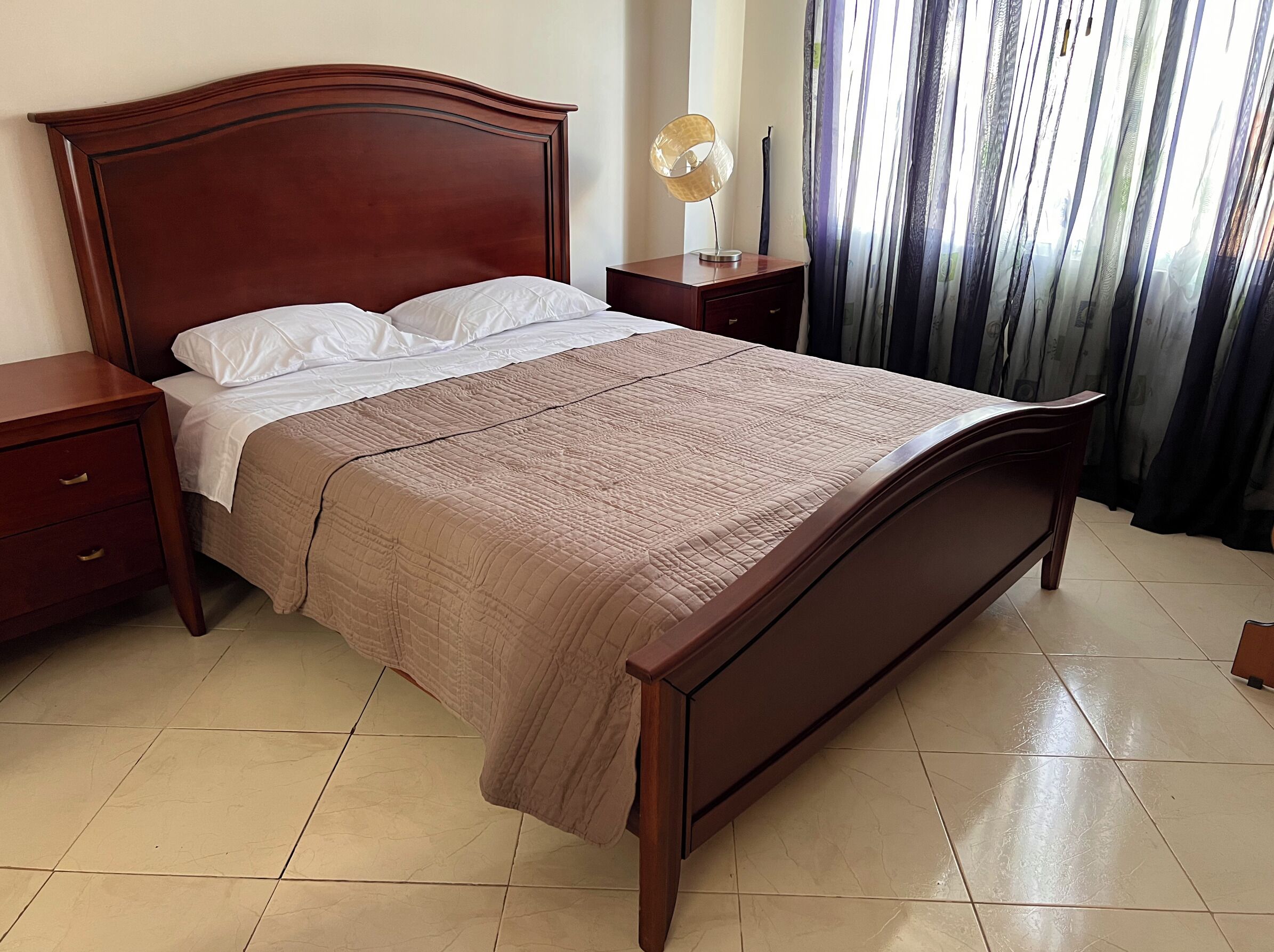 Uma cama bem arrumada com cabeceira de madeira, mesa de cabeceira e uma luminária.