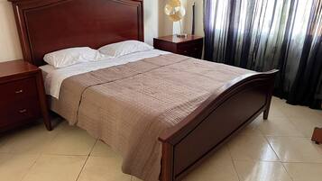 Uma cama bem arrumada com cabeceira de madeira, mesa de cabeceira e uma luminária.