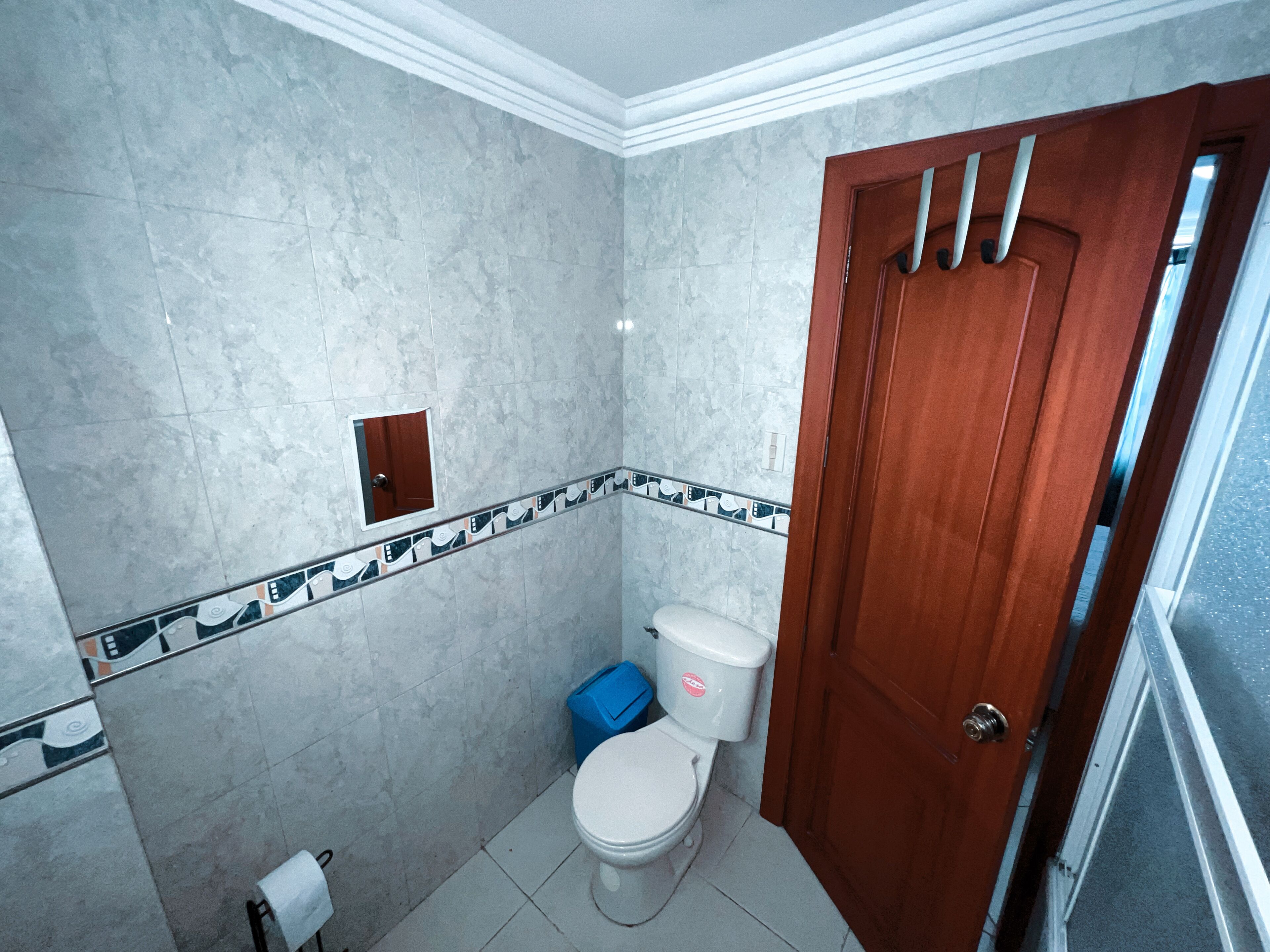 Ein Badezimmer mit Toilette, einer blauen Mülltonne, einem Handtuch und einer Holztür.