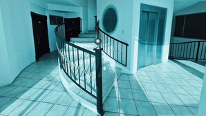 A spacious hallway with a curved staircase, a round mirror, and a door leading to an elevator. - Departamento Centrico en Loja (Loja)