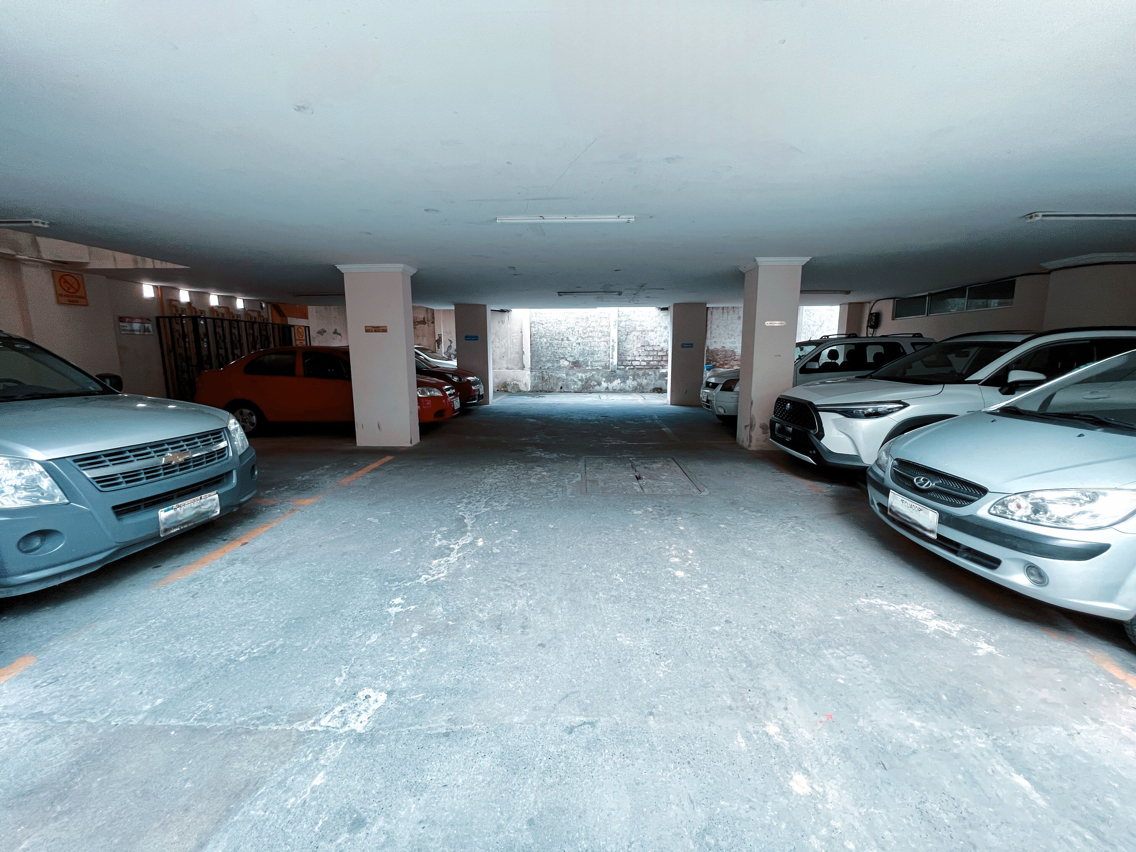 A parking garage with multiple cars parked in rows, concrete pillars, and a visible exit.