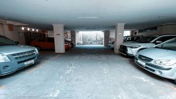 A parking garage with multiple cars parked in rows, concrete pillars, and a visible exit.