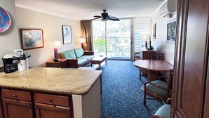 A hotel room with a kitchen, a dining area, a living area with a sofa, and a balcony with a view.