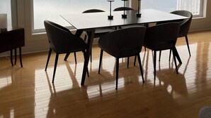 A dining area with a table and chairs, large windows with a view of the sea, and a white railing outside. - Sunset Retreat Awaits (Big Pond)