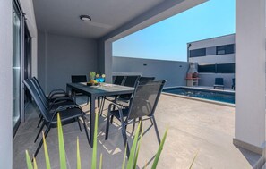 En udendørs terrasse med pool, et bord med stole og en pizzovn.