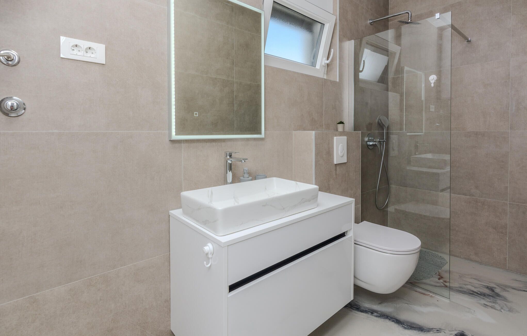 Une salle de bain moderne avec un lavabo blanc, des toilettes et une douche à parois de verre.
