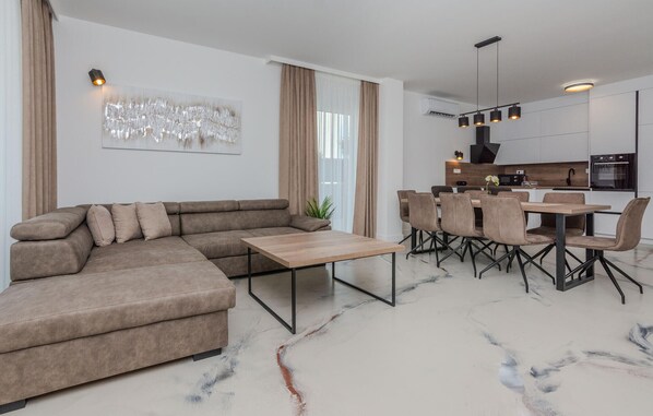 A modern living room with a sectional sofa, a dining table with chairs, a kitchen area, and a large abstract painting on the wall. - Luxurious home in Vrsi (Vrsi)