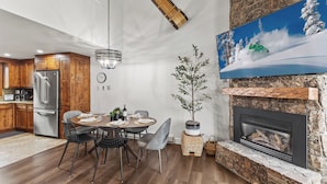 A modern kitchen with wooden cabinets, a stainless steel refrigerator, and a dining area with a round table and chairs. - Mountain modern-At the base (Steamboat Springs)