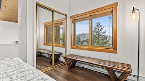 A bedroom with a large mirror, wooden bench, and a view of trees and mountains through a window. - Mountain modern-At the base (Steamboat Springs)