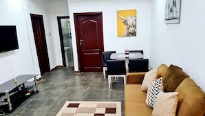 Una sala de estar con sofá, una mesa de centro, un televisor y una puerta que da a un baño.