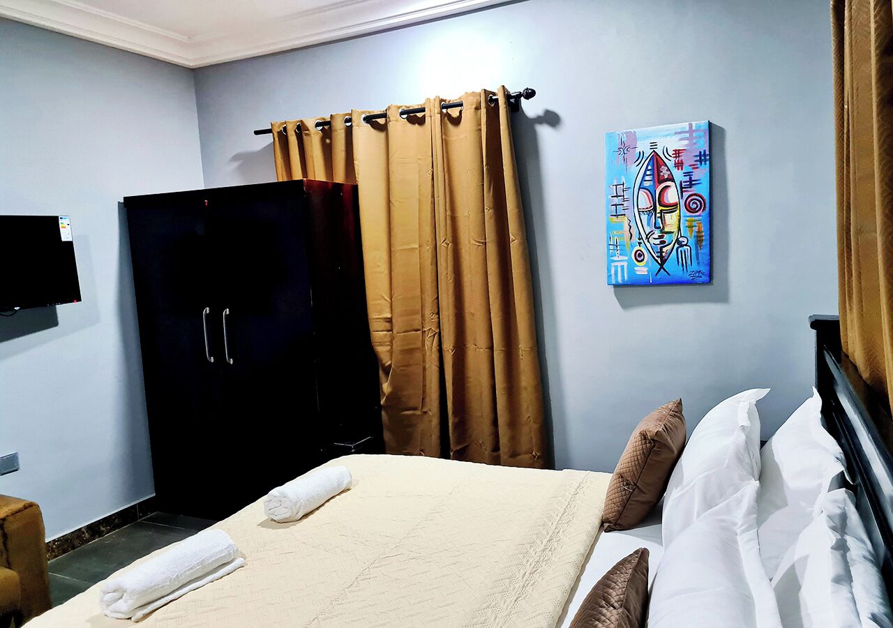 A hotel room with a bed, a wardrobe, a painting on the wall, and a curtain.