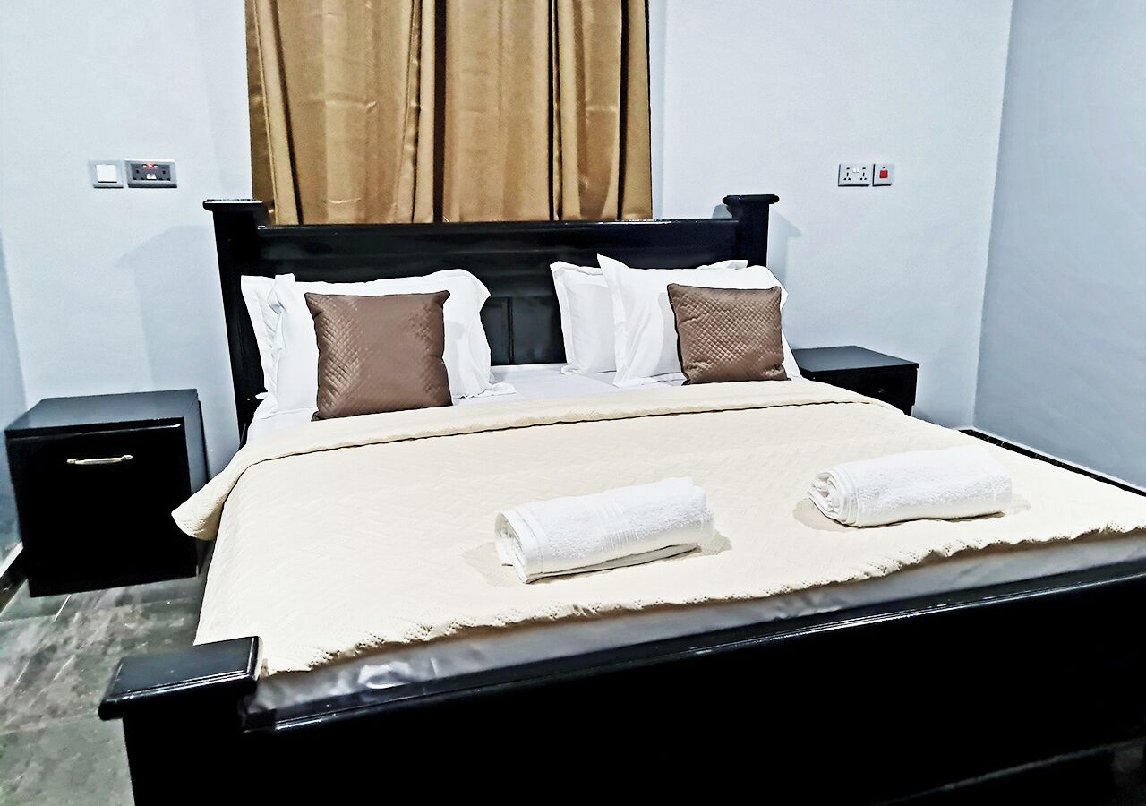 A neatly made bed with white and brown pillows, a beige bedspread, and two folded white towels.