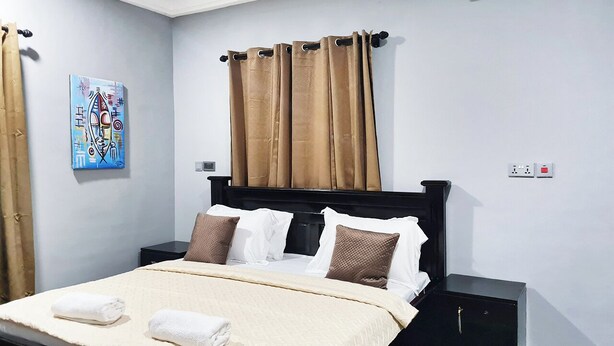 Una cama bien tendida con ropa de cama blanca y marrón, un cabecero negro y una mesita de noche.