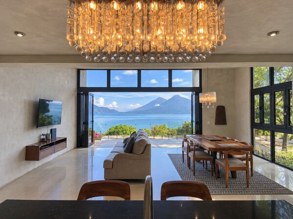 A modern living room with a large window, a chandelier, a sofa, and a dining area.