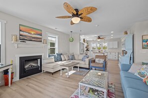 A spacious living room with a fireplace, a ceiling fan, and a kitchen in the background.