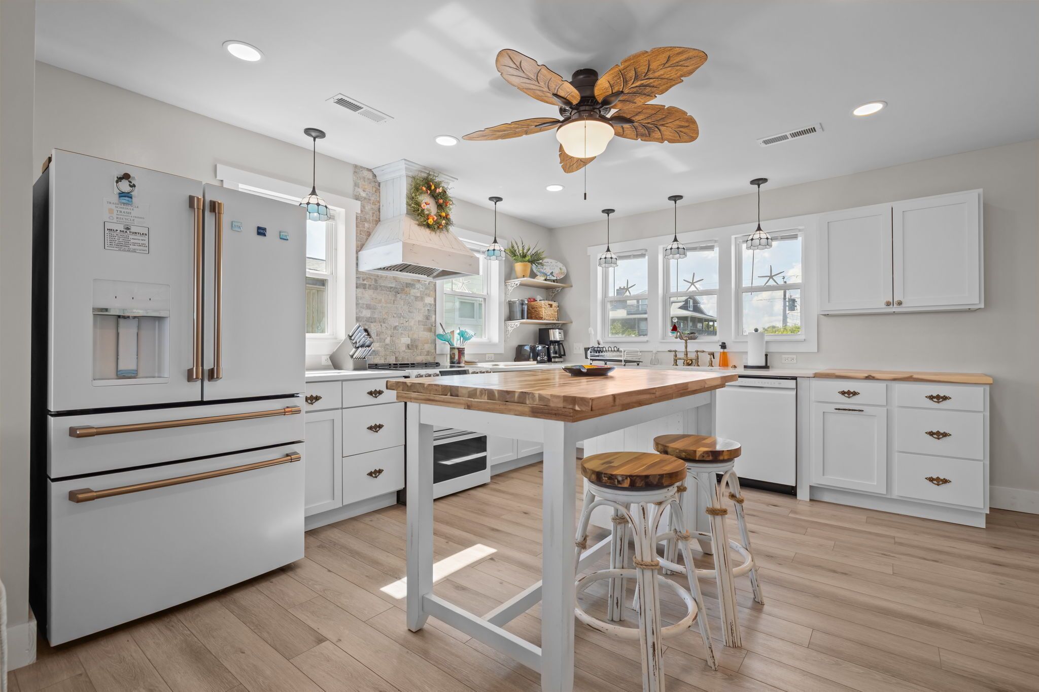 Une cuisine moderne avec des meubles blancs, un îlot central en bois et un ventilateur de plafond.