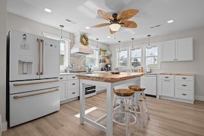 A modern kitchen with white cabinetry, a wooden island, and a ceiling fan.