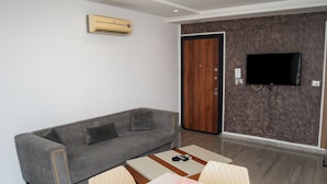 A living room with a grey sofa, a coffee table, and a TV mounted on the wall. - Residence Mami (Gabes)