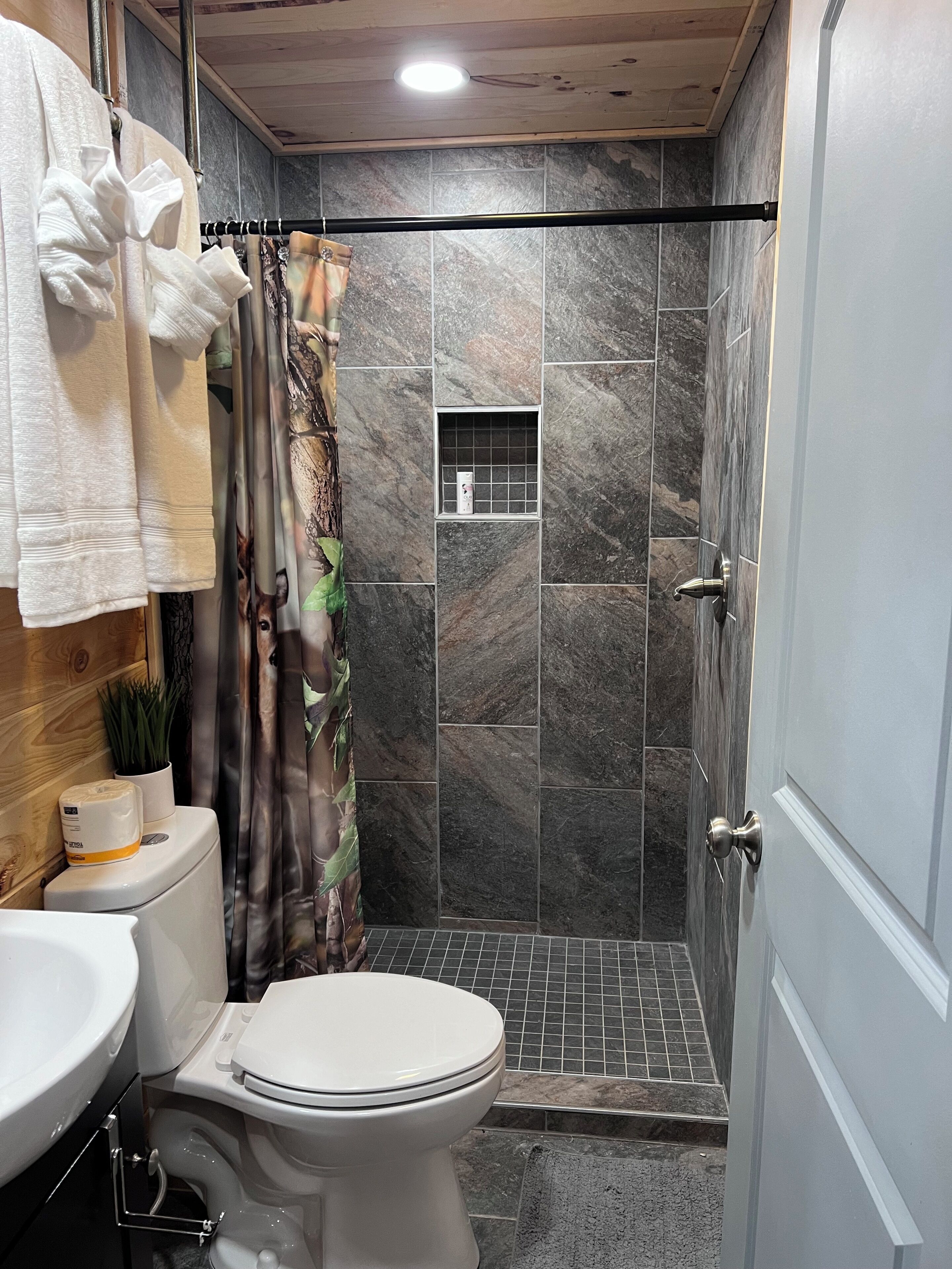 A bathroom with a toilet, sink, shower, and a small window.
