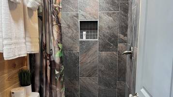 A bathroom with a toilet, sink, shower, and a small window.