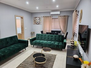 A living room with a green sofa, a dining table, and a TV. - Spacious Luxury 3Bed Hse in Tema Netflix (Tema)