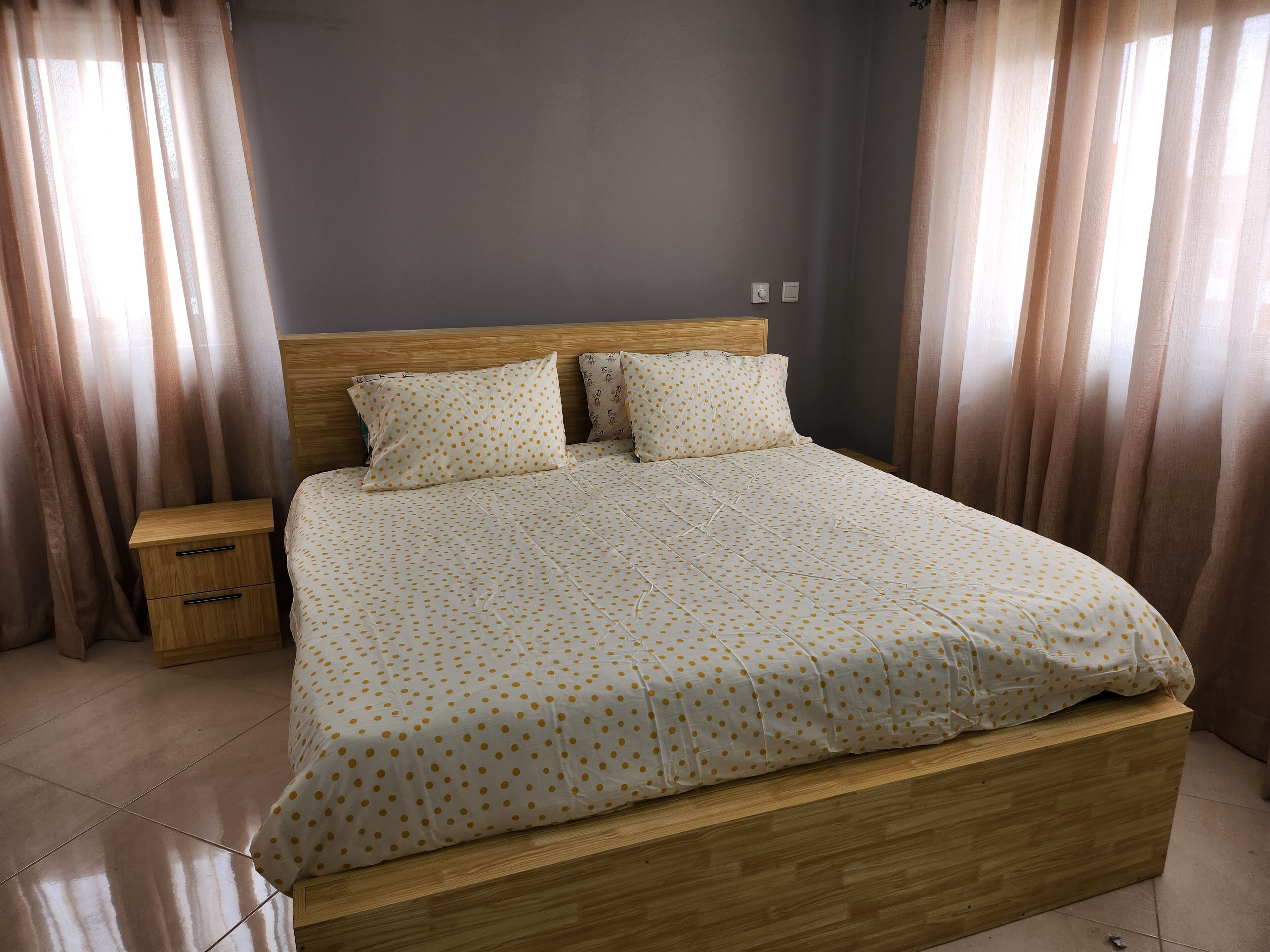 A neatly made bed with a polka dot bedspread, a wooden headboard, and a nightstand with a drawer.