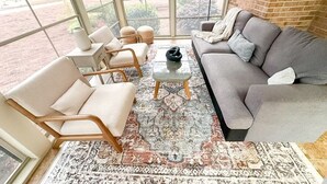 Ein Wintergarten mit einem grauen Sofa, beigen Sesseln und einem gemusterten Teppich.