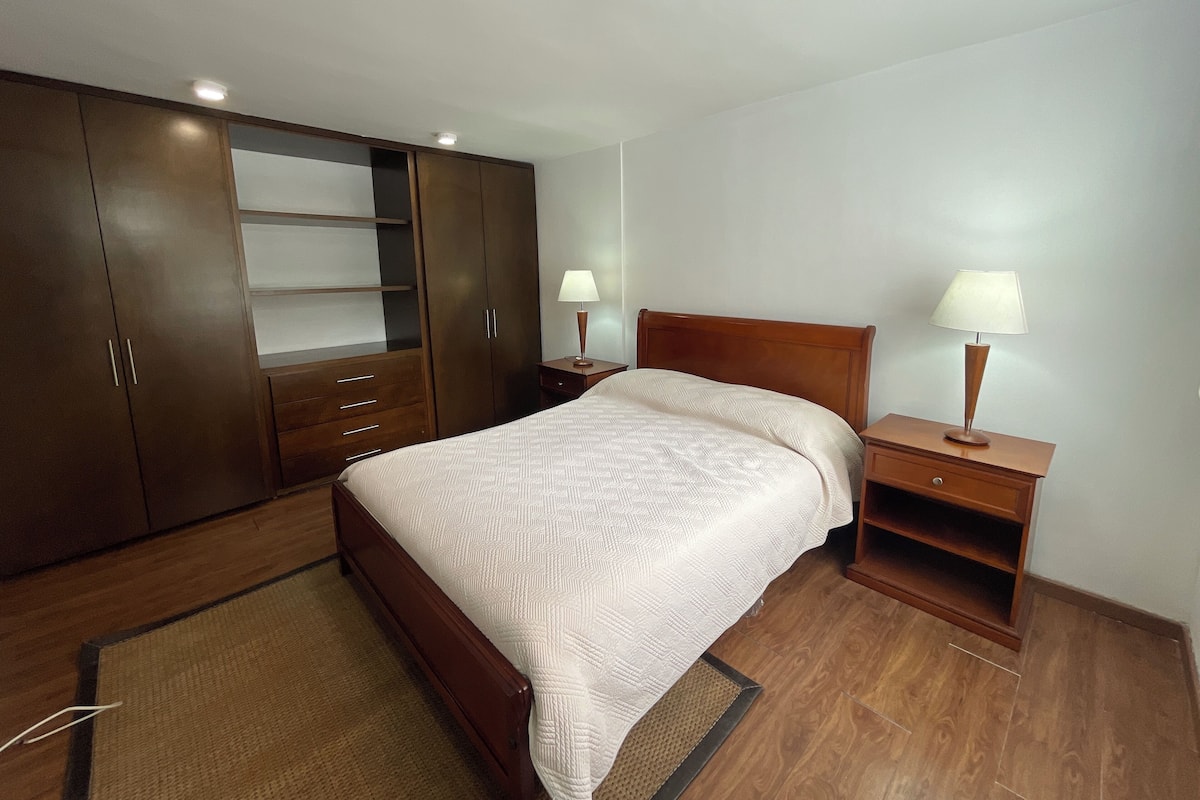 Une chambre dotée d’une grande armoire, d’un lit recouvert d’une couvre-lit à motifs, de deux tables de chevet avec des lampes et d’un plancher en bois.