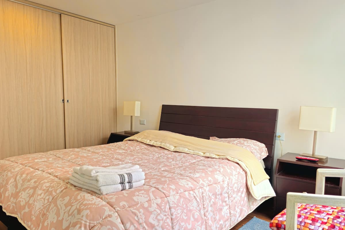 Un lit bien fait, recouvert d’une couvre-lit à motifs floraux roses, et une serviette blanche pliée posée sur le bord.