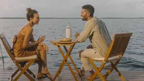 Two people seated at a wooden table on a dock with a view of the water. - Premium Floating Bugalow by Stay Ombi in the Keys with Stunning Ocean Views. (Key Largo)