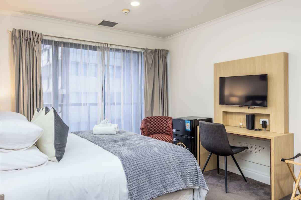 Une chambre d’hôtel équipée d’un lit, d’un bureau, d’une chaise, d’une télévision et d’une fenêtre avec des rideaux.