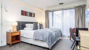 A modern hotel room with a bed, bedside table, desk, chair, and large window with curtains. - Highrise studio w AC, Pool and Gym in Auckland CBD (Auckland)