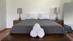 A neatly made bed with a grey quilt, two white pillows, and rolled white towels in front.
