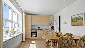Une cuisine moderne avec des meubles en bois, un coin repas avec des chaises en osier et une vue sur la mer grâce à de grandes fenêtres.
